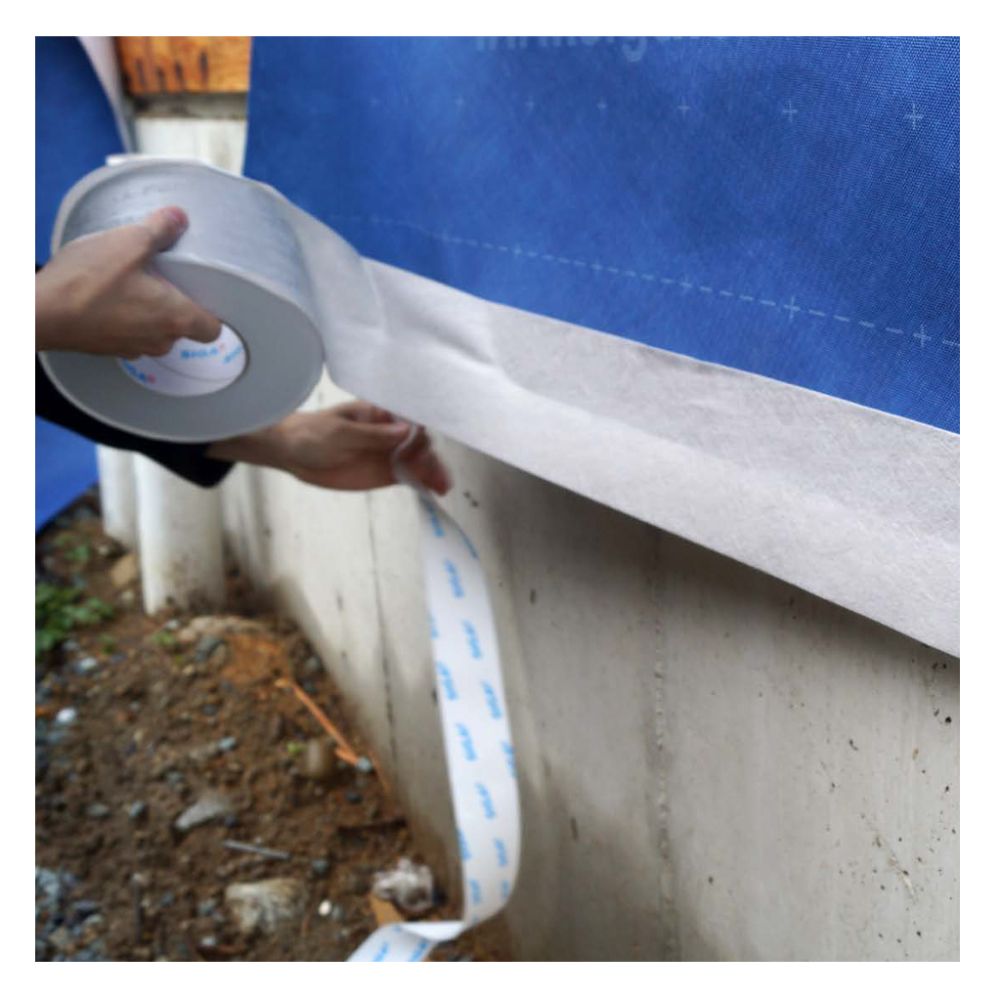 Application of an extra-wide 9-inch roll of Fentrim 430 grey joint sealing tape to a concrete foundation for a robust, airtight exterior seal.
