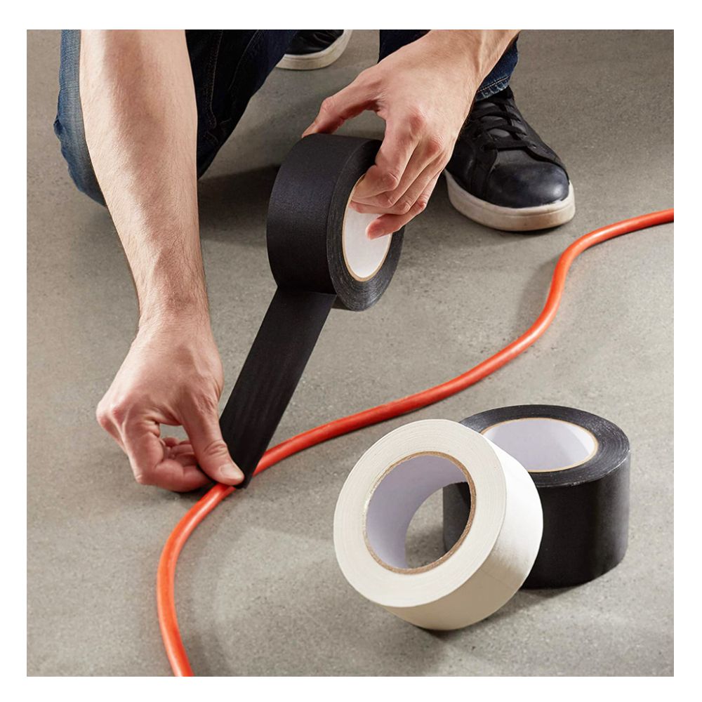 Person applying black cloth gaffer tape to secure an extension cable to the floor