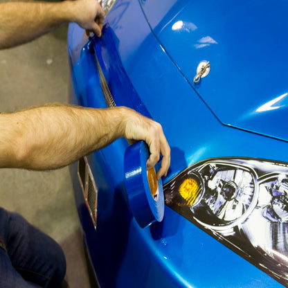 Close-up of a technician applying high-adhesion blue Shurtape duct tape to a blue racing vehicle body for temporary repairs