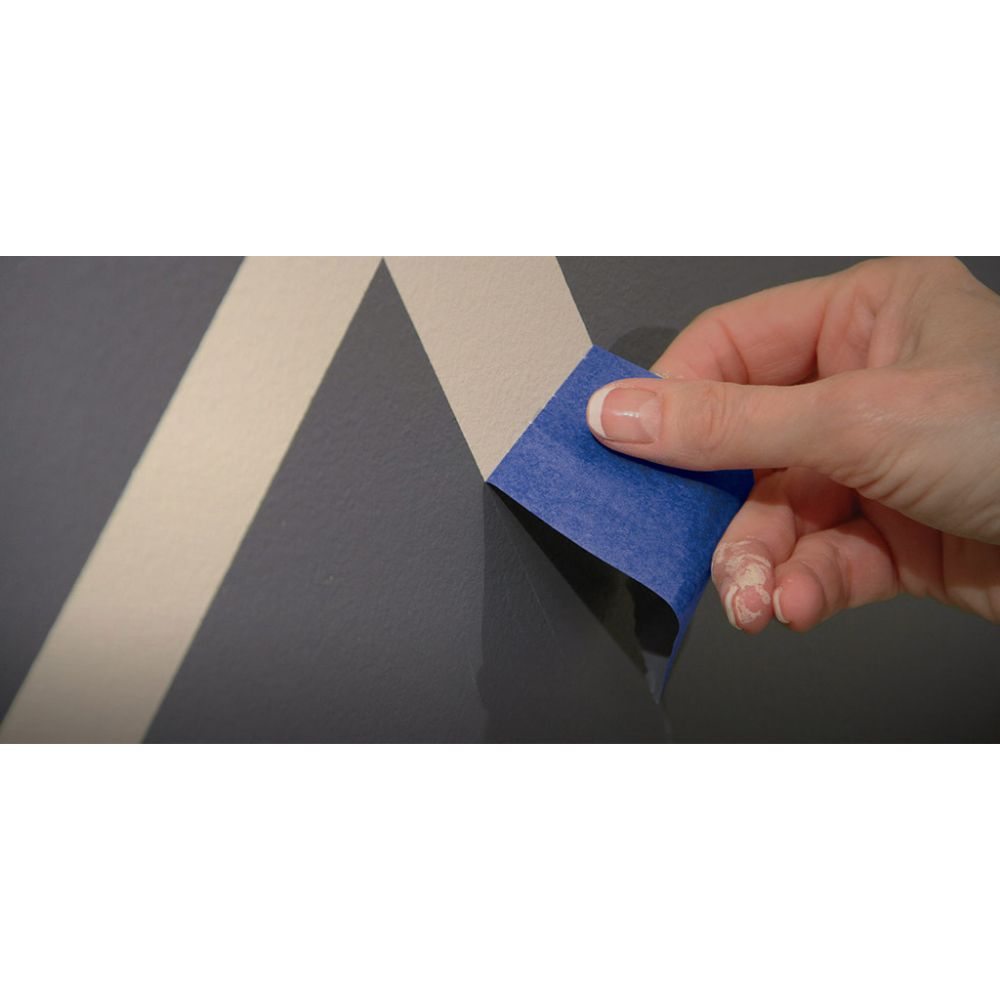Hand peeling back dark blue painter's tape to reveal sharp geometric paint lines on a wall.