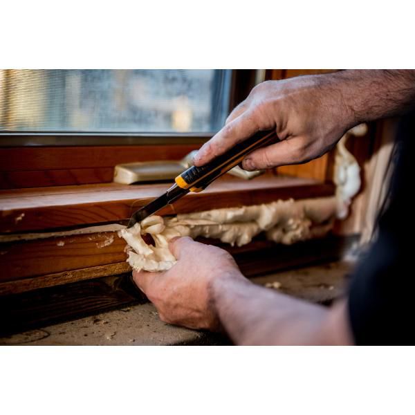 Worker using a sharp snap off utility knife to neatly trim expanded polyurethane insulation foam sealant from a wooden window sill