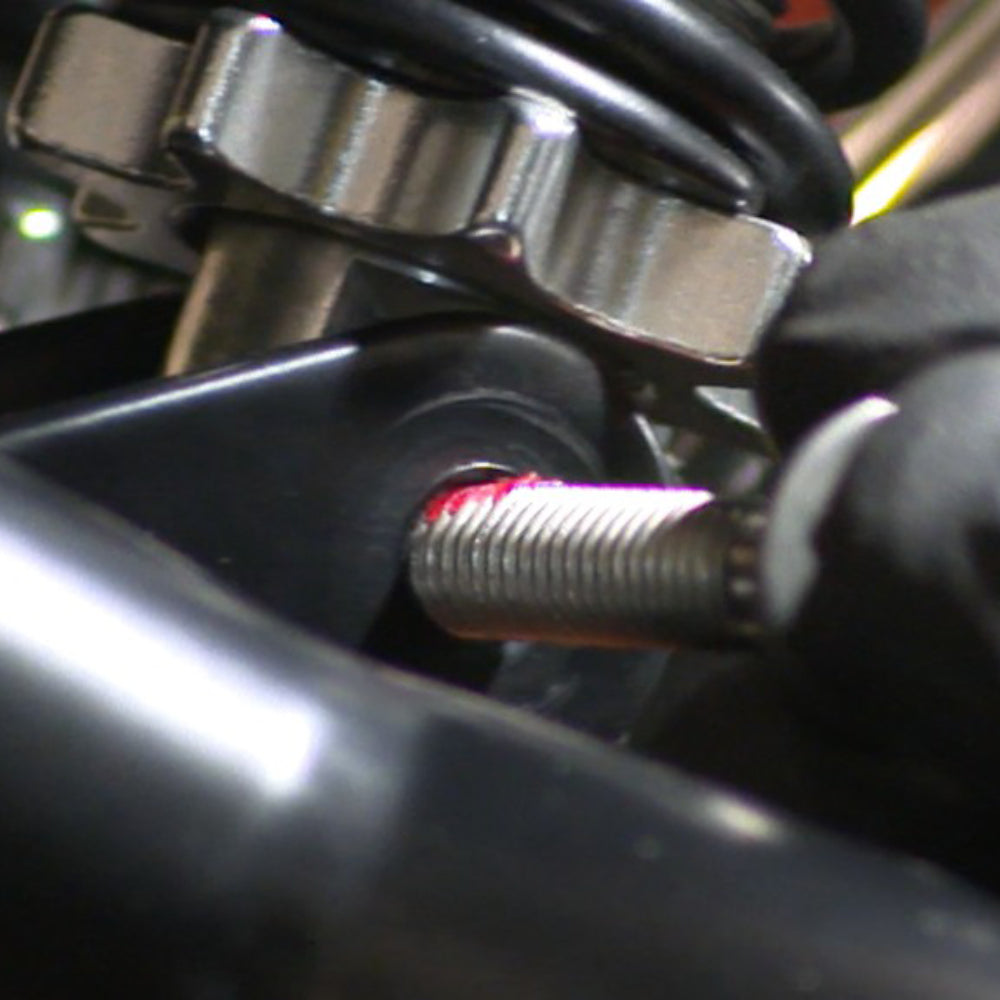 Close-up of red Loctite threadlocker applied to metal bolt threads in an automotive engine or industrial machinery assembly showing cured adhesive on fastener threads