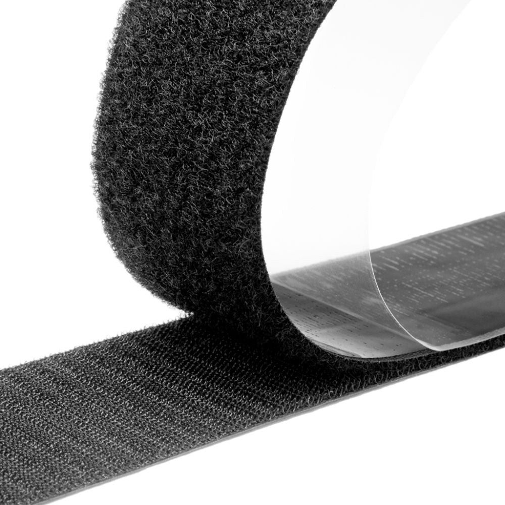 Close-up view of a black C1-L loop fastener tape showing the dense, fuzzy loop texture and a clear adhesive backing liner peeling away on a white background.
