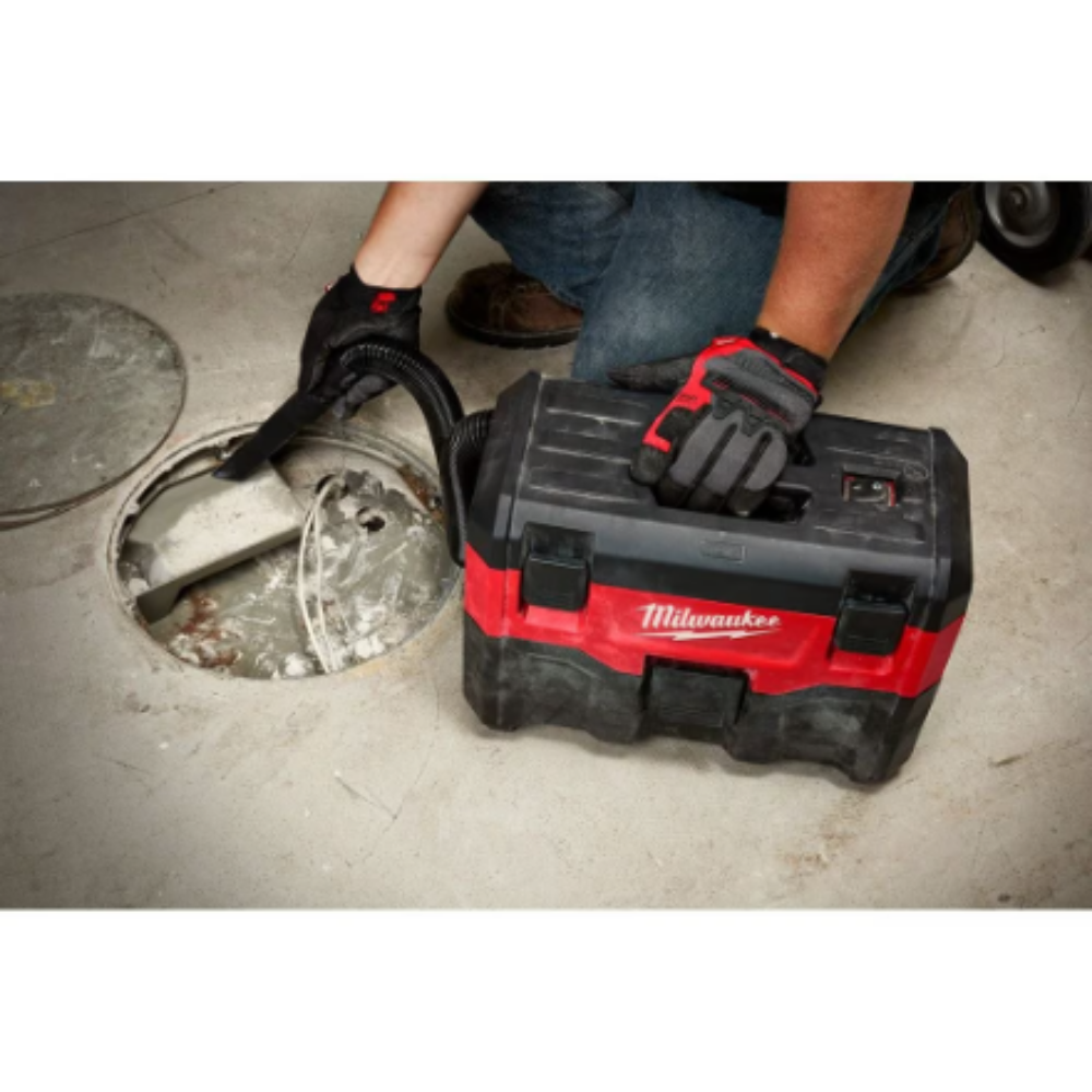 A worker wearing protective safety gloves uses the Milwaukee 0880-20 M18 cordless wet dry vacuum crevice tool attachment to clean a concrete floor drain basin.
