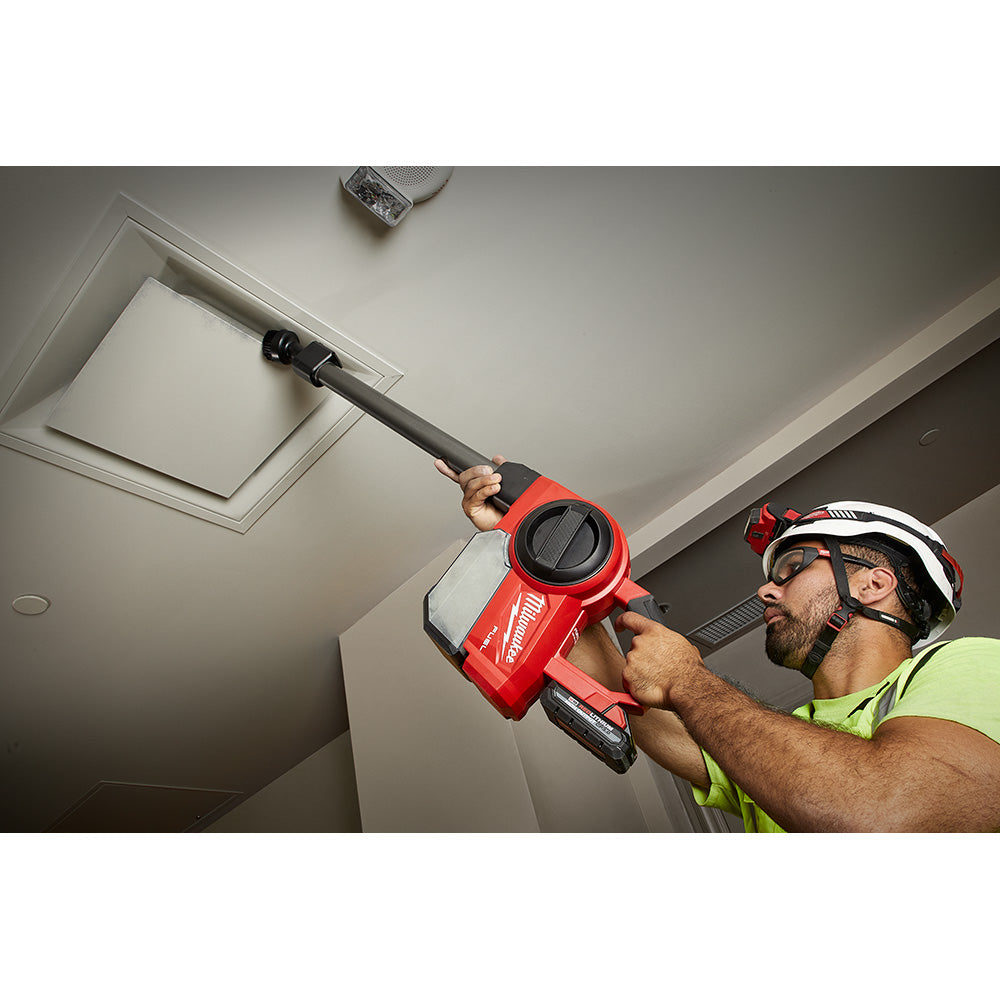 Worker using Milwaukee M18 FUEL cordless compact vacuum with extension wand to clean ceiling vent on job site