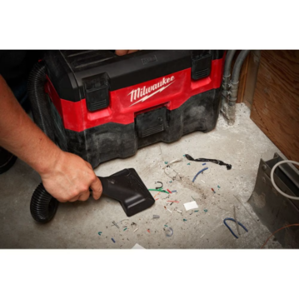 Close-up of a worker using the wide utility nozzle attachment on the Milwaukee M18 0880-20 portable vacuum to clean wire clippings and debris off a concrete workshop floor.