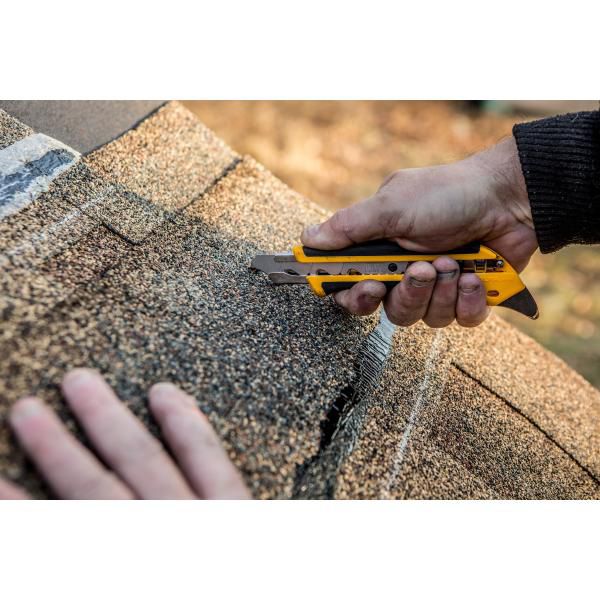 Flooring installer using an ergonomic yellow OLFA utility knife to cleanly trim the edge of a thick textured carpet near a baseboard