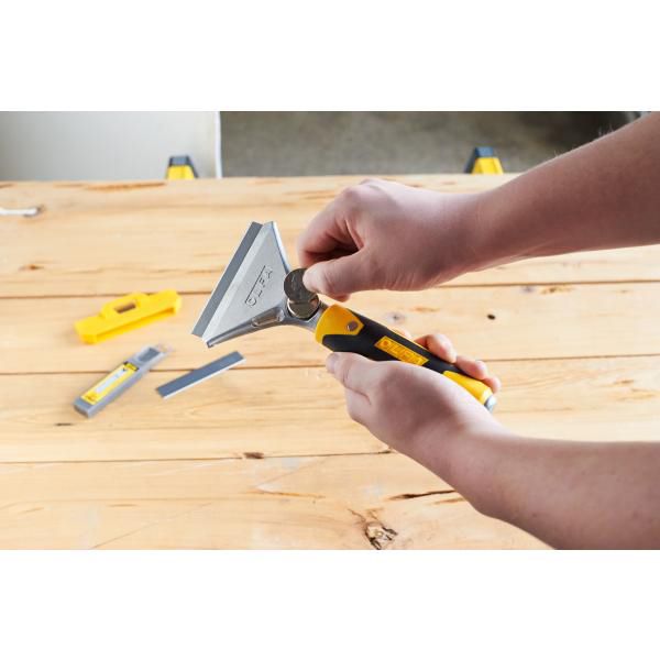 Hands changing blade on Olfa heavy duty scraper with yellow black ergonomic handle on wood workbench
