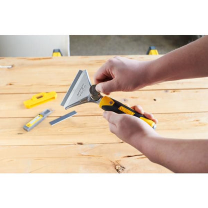 Hands changing blade on Olfa heavy duty scraper with yellow black ergonomic handle on wood workbench