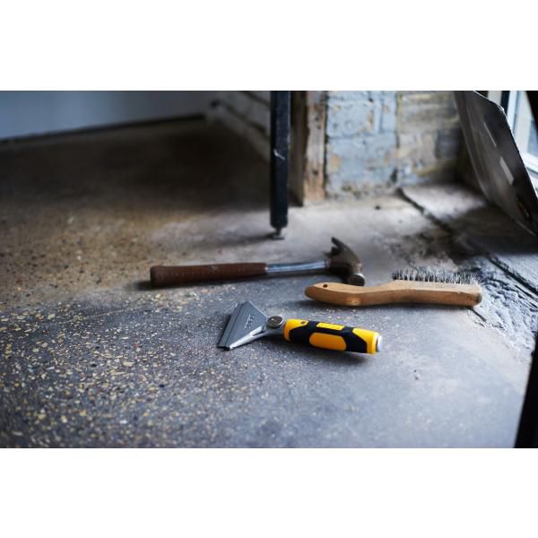 Olfa heavy duty scraper with yellow black handle placed on concrete floor beside hammer and brush
