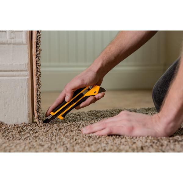 Close up view of a worker using a yellow and black OLFA utility knife to precisely cut heavy duty asphalt roofing shingles