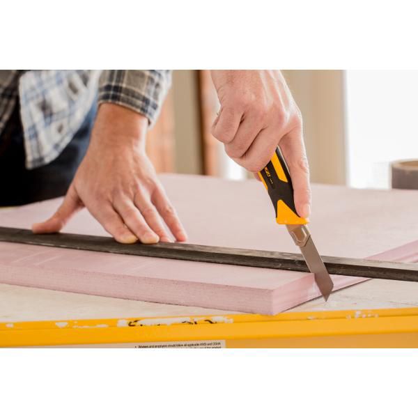 Precision cutting of a pink rigid foam insulation board with an OLFA utility knife guided along a straight edge ruler