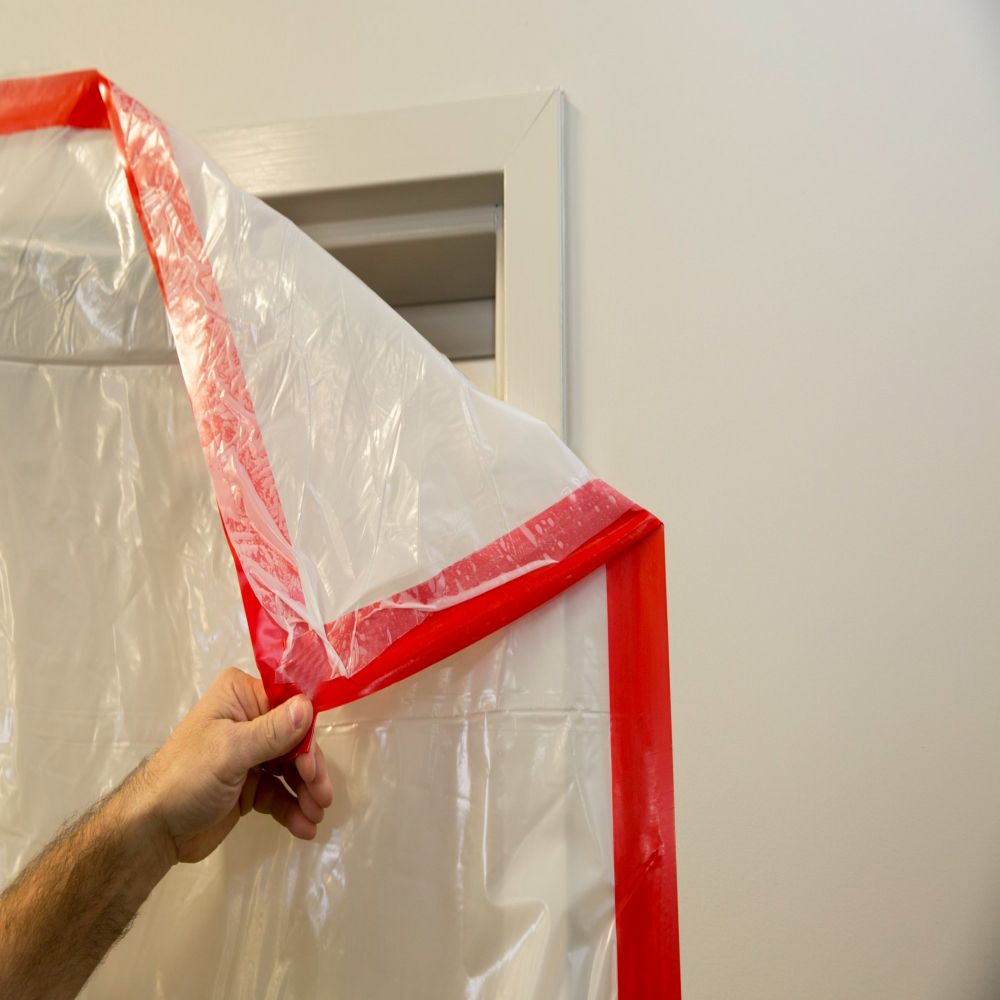Detailed view of red PE444 UV-resistant tape being applied to mask a door frame, demonstrating its clean removal and high-visibility properties for surface protection.