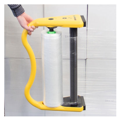 Close-up of a hand holding the ergonomic handle of the yellow Precision Wrap XL tool while dispensing clear plastic wrap onto stacked white shipping containers