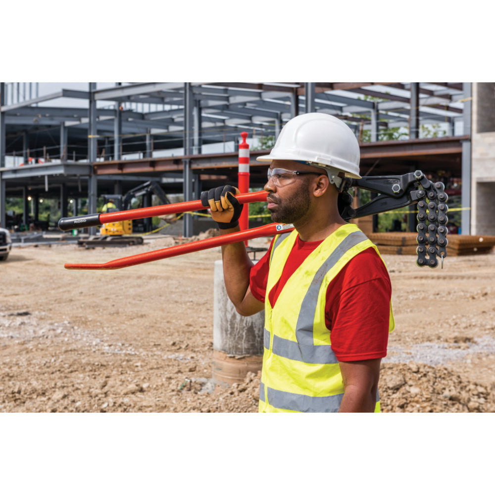 Construction worker in gloves turning the adjustment knob of a RIDGID 286 soil pipe cutter clamped to a pipe on dirt ground.