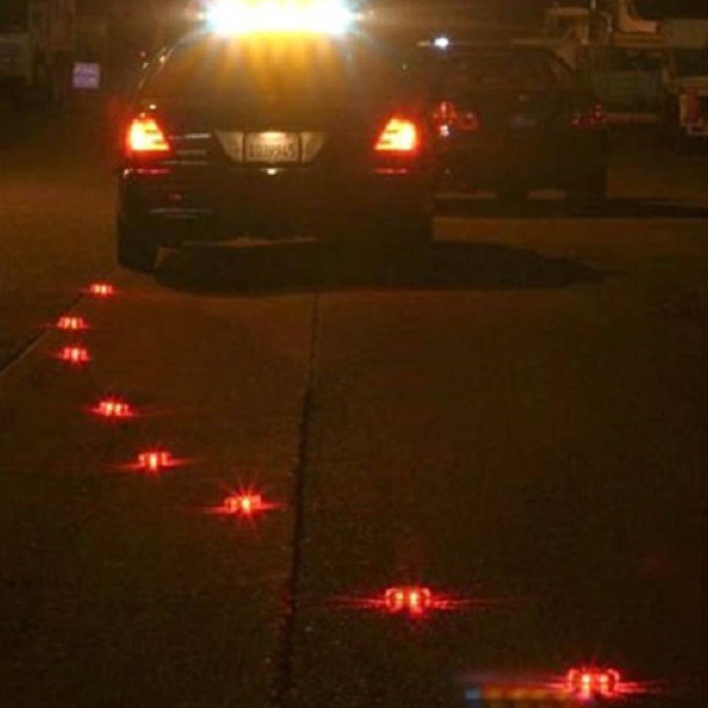 Multiple red and orange LED safety flares deployed in a line on a dark road behind a vehicle to direct traffic during an emergency.