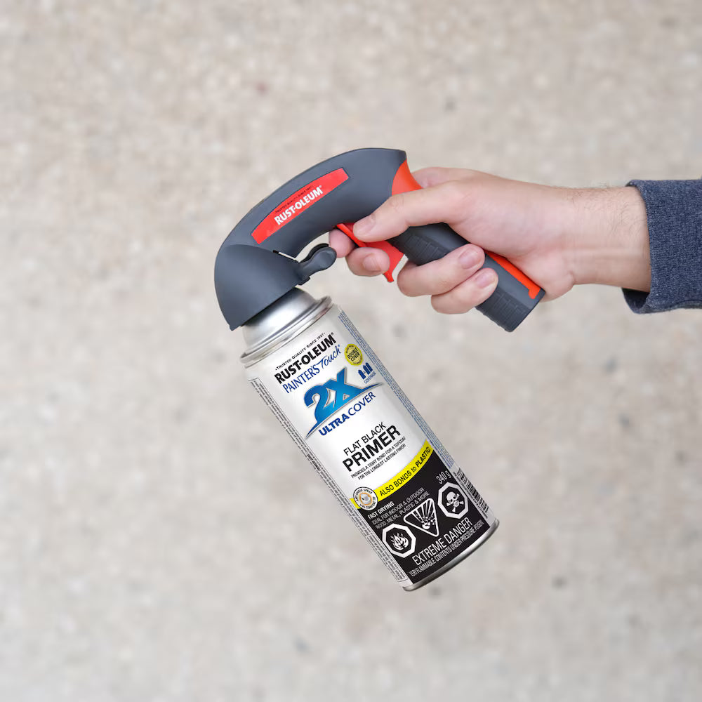 Hand holding a Rust-Oleum flat black primer aerosol spray can with an ergonomic black and red Comfort Grip spray trigger handle attached.