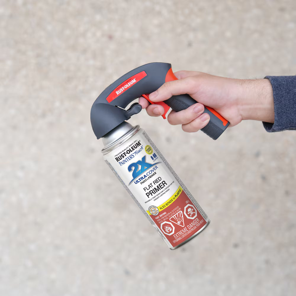 A hand holding a Rust-Oleum flat red primer spray paint can equipped with an ergonomic red and black Rust-Oleum Comfort Grip trigger handle attachment.