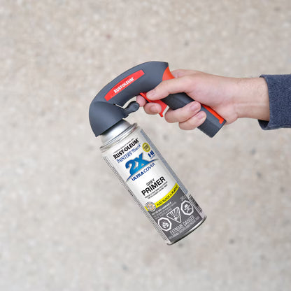 A hand holding a Rust-Oleum grey primer spray paint can equipped with an ergonomic red and black Rust-Oleum Comfort Grip trigger handle attachment.