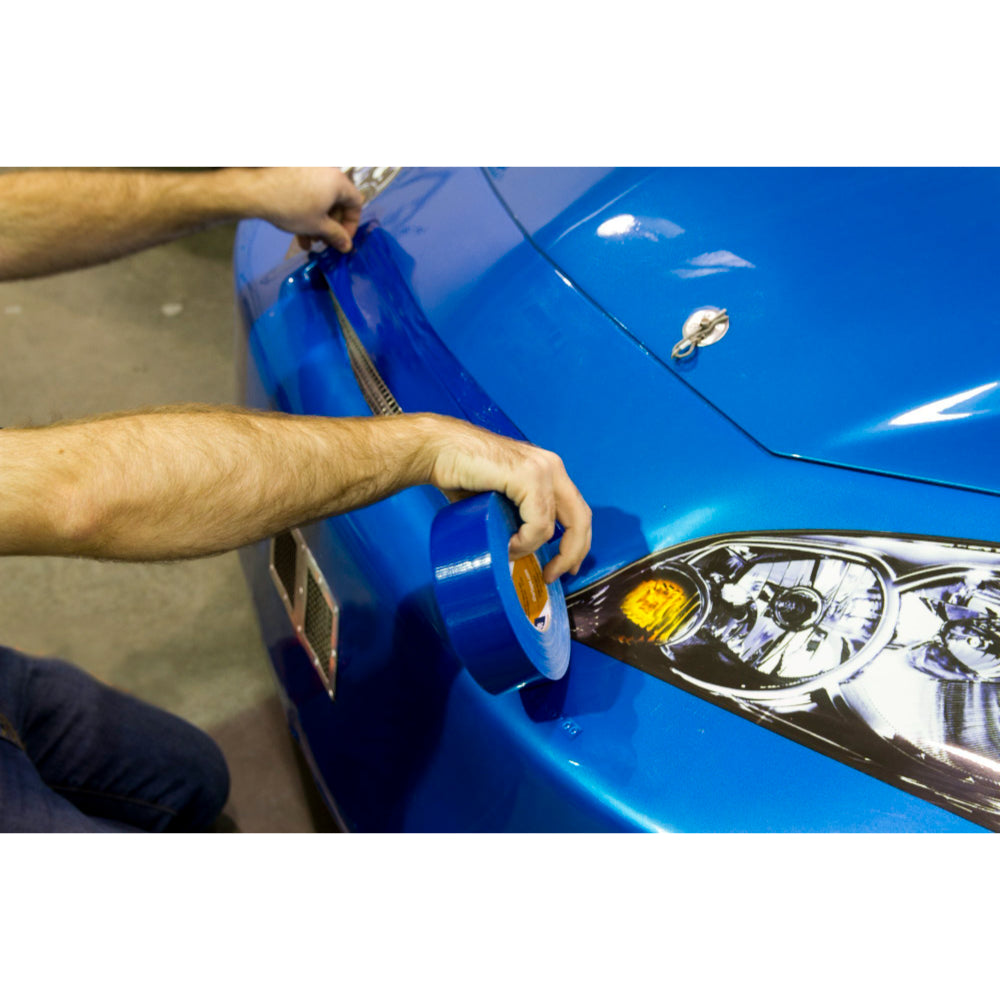 Person applying blue Shurtape gaffer tape to a car hood for surface protection and racing maintenance.
