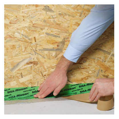 Close-up of green Rissan reinforced sealing tape being applied by hand to seal the junction between an OSB wall panel and a concrete floor for airtightness.