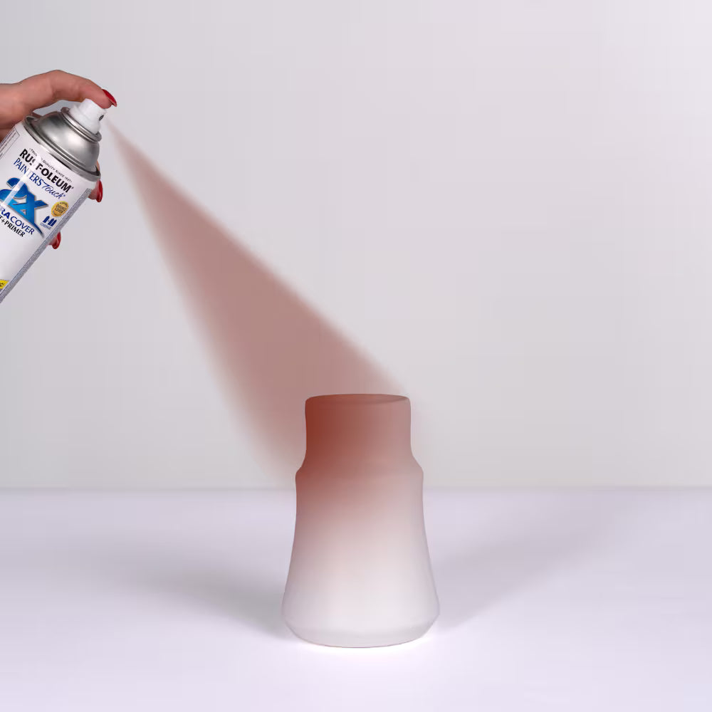 Close-up of a hand using a Rust-Oleum Painter's Touch spray can to apply a smooth coat of red primer onto a white ceramic vase.