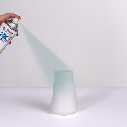 Close-up of a hand using a Rust-Oleum Painter's Touch spray can to apply a smooth coat of grey primer onto a white ceramic vase.
