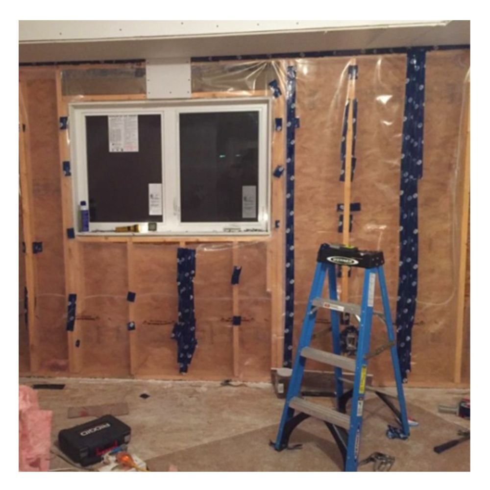 Interior construction view showing blue Tuck 219 vapour barrier tape sealing vertical seams of polyethylene film over wall insulation.
