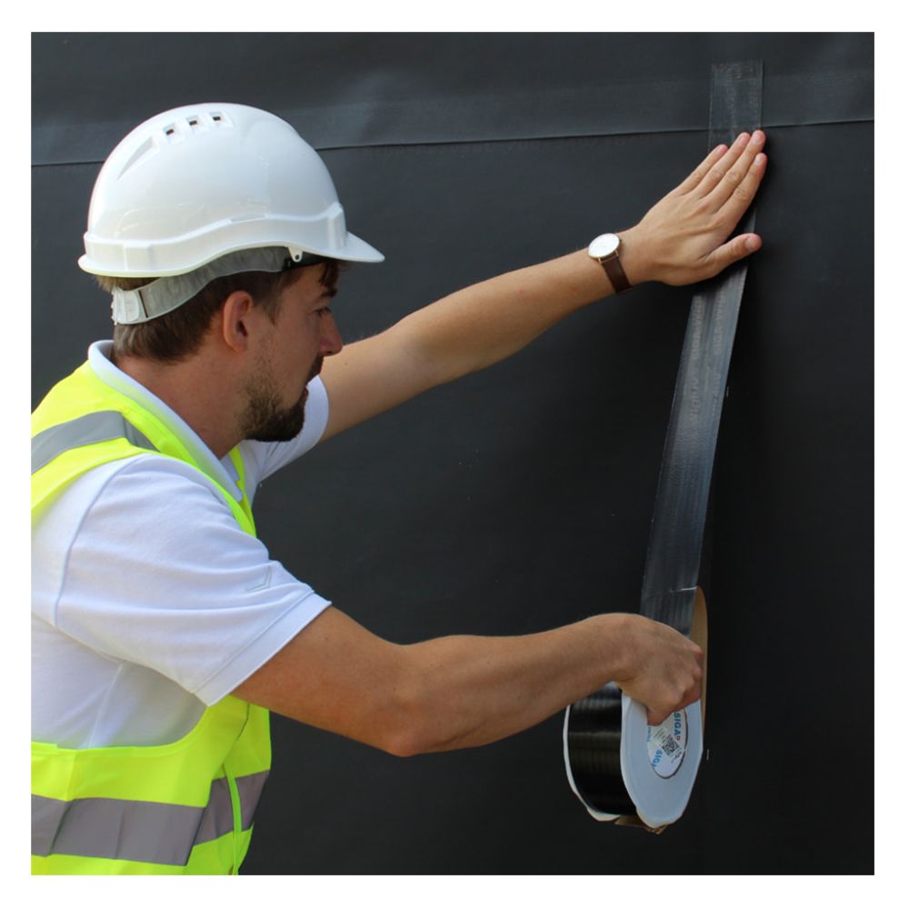 Contractor applying black Wigluv 60 UV-resistant sealing tape to an exterior weather barrier to create a permanent airtight and rainproof joint.