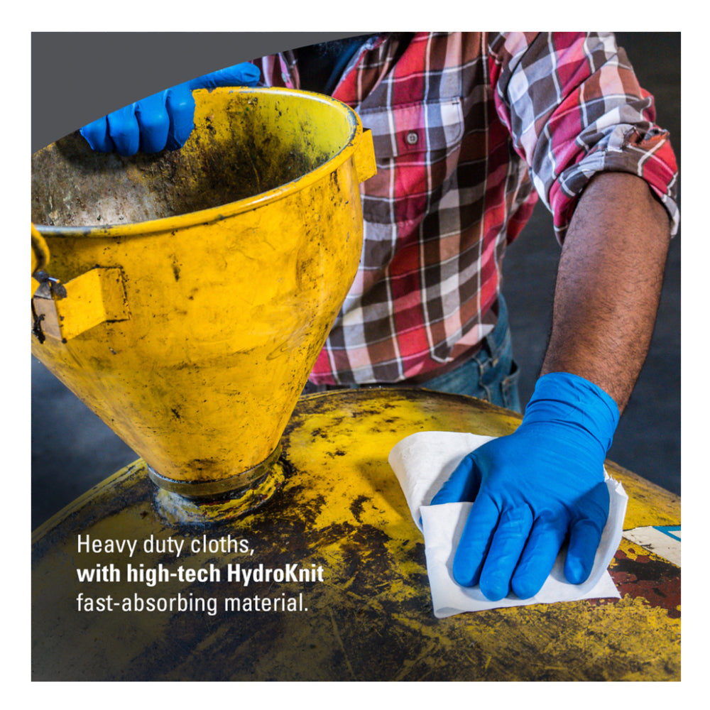 A worker wearing blue nitrile gloves uses a white WypAll heavy-duty cloth made of fast-absorbing HydroKnit material to wipe grease off a yellow industrial machine
